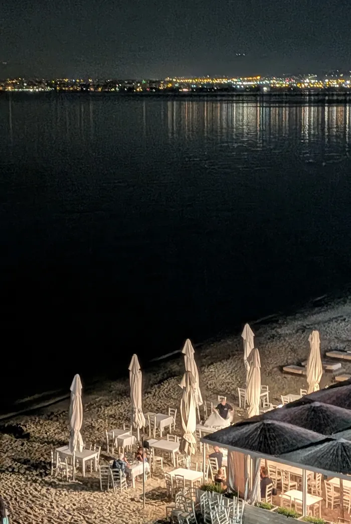 Beachfront tables in Perea at night, with Thessaloniki’s lights across the bay