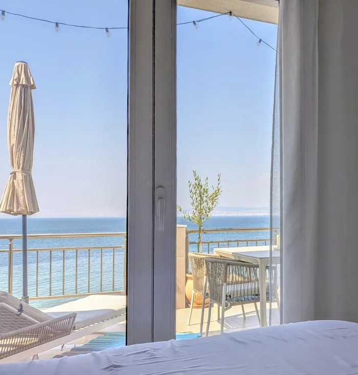 View from the bed through the balcony door to the terrace and the sea