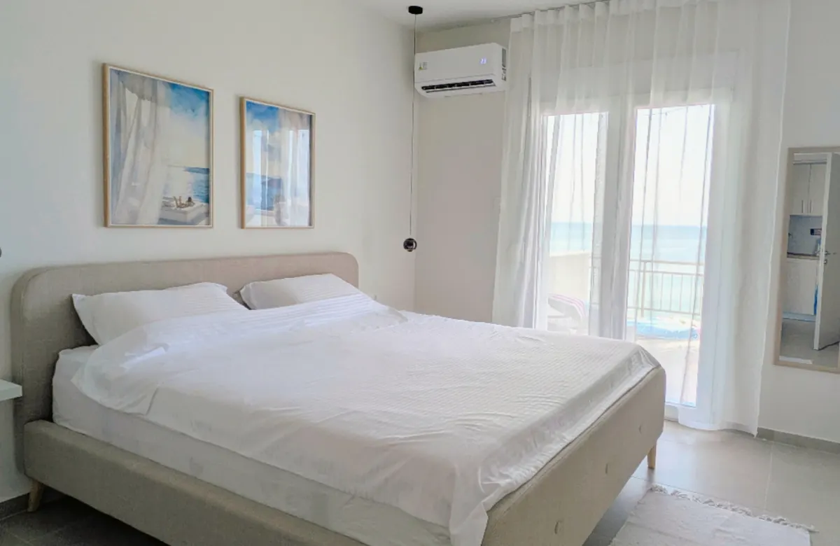 Bedroom with a large bed, sheer curtains and a balcony door onto the sea