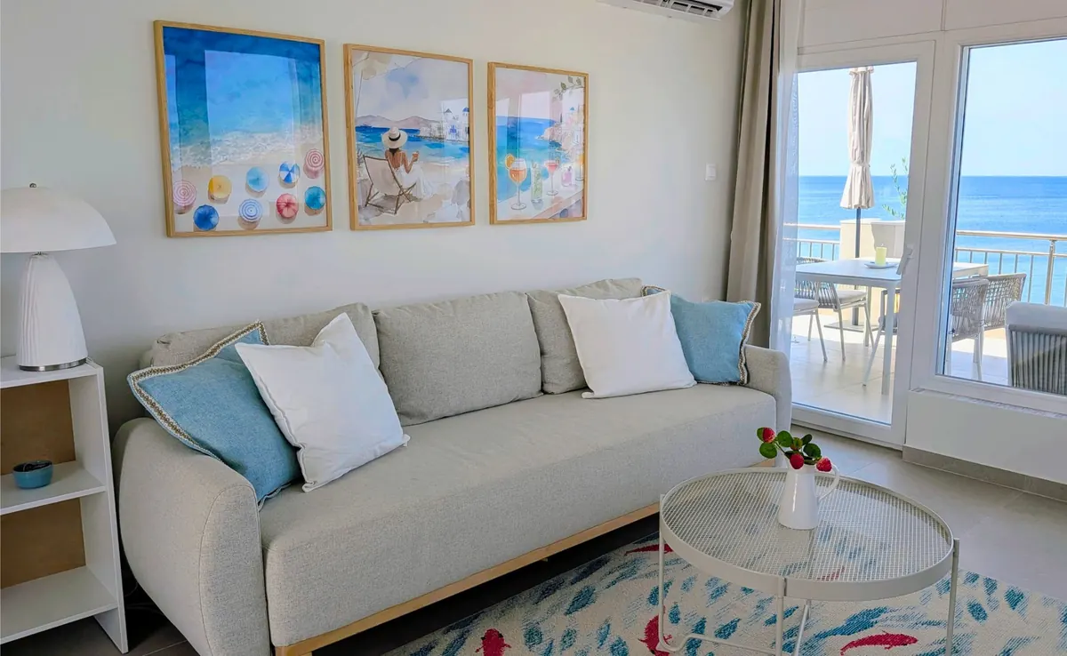 Living room with a soft grey sofa, sea-themed art and a window onto the terrace