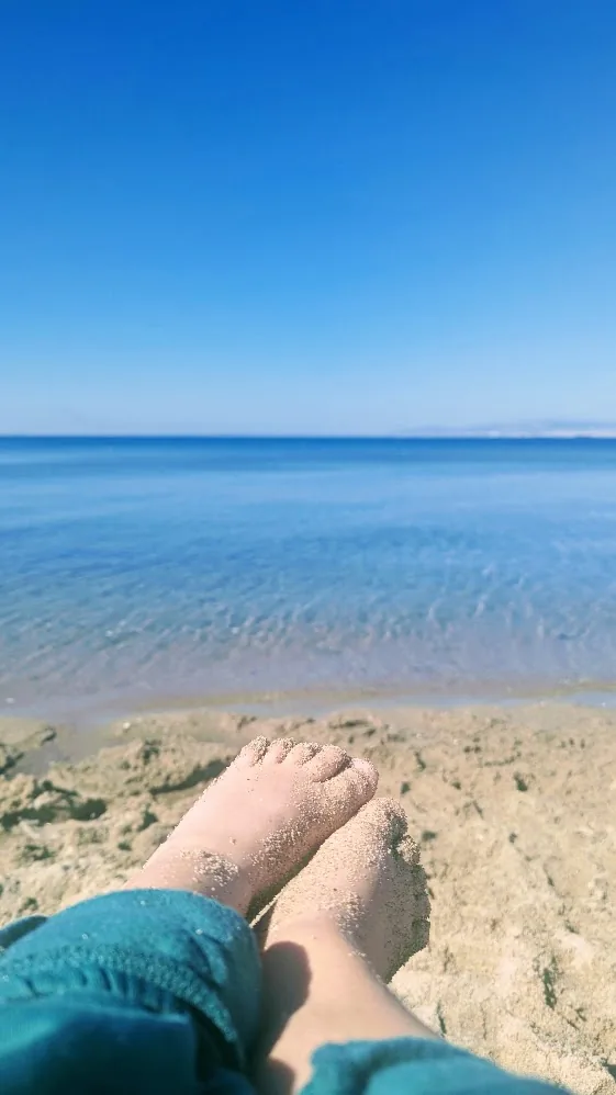 Bare feet in the warm sand at the water’s edge on Perea beach