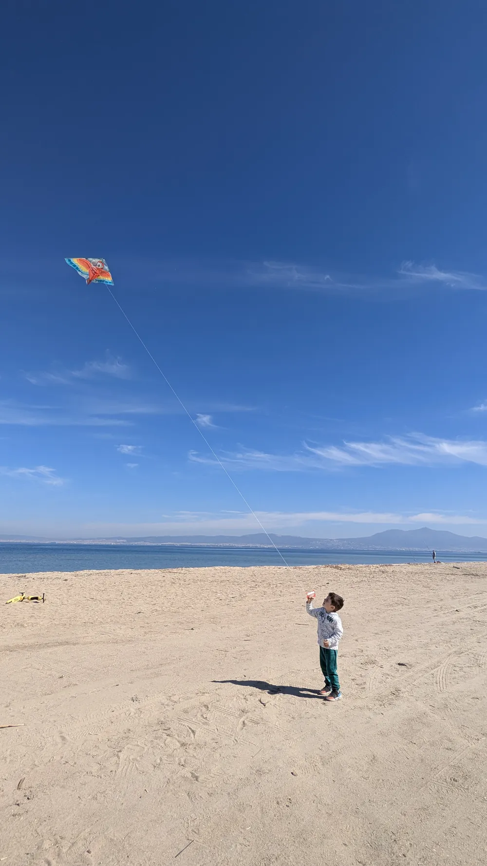 A child flying a kite on the wide sandy beach in Perea