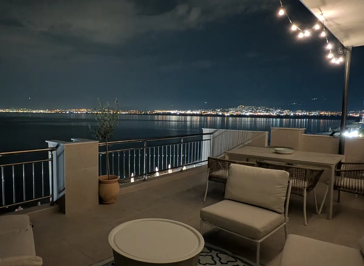 The terrace at night under string lights, with the lights of Thessaloniki across the bay